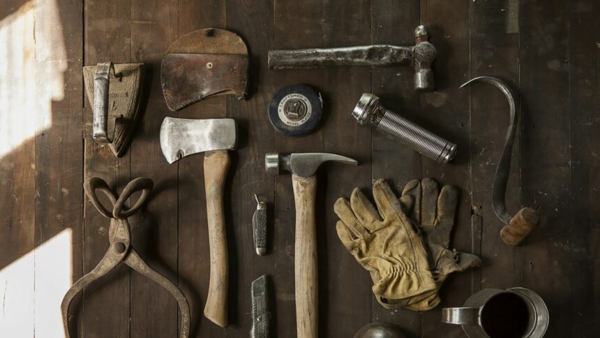 Worn hand tools and leather work gloves laid out on a wooden bench