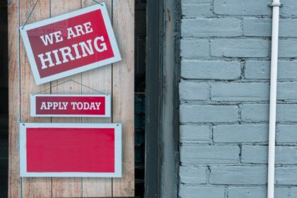 Hiring sign taped to a brick wall beside an apply today notice