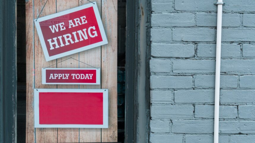 Hiring sign taped to a brick wall beside an apply today notice