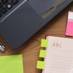 A laptop, an open notebook and a pen on a wooden desk