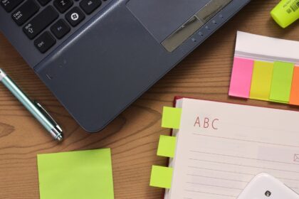 A laptop, an open notebook and a pen on a wooden desk