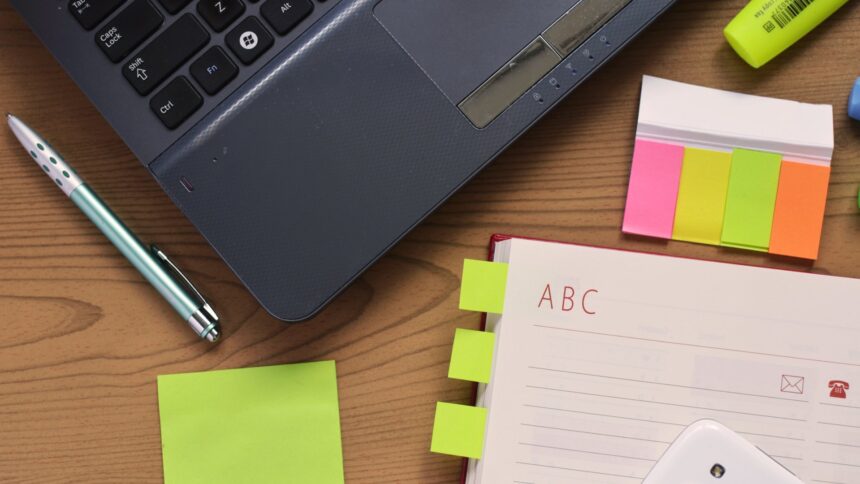 A laptop, an open notebook and a pen on a wooden desk