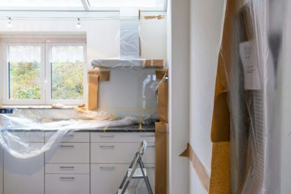 Kitchen with white cabinets covered in plastic sheeting during a renovation
