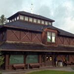Dark log-faced Banff Park Museum with a tiered shingle roof and a lantern, seen across a lawn with evergreen trees