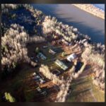 Aerial view of a scatter of small buildings on a riverbank among dry grass, with the river beside them