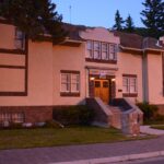 Two-storey buff stucco building with brick trim, a COURT HOUSE sign over the entrance, shaped parapet gables and a tiled roof, photographed at dusk