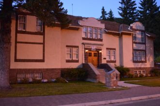 Two-storey buff stucco building with brick trim, a COURT HOUSE sign over the entrance, shaped parapet gables and a tiled roof, photographed at dusk