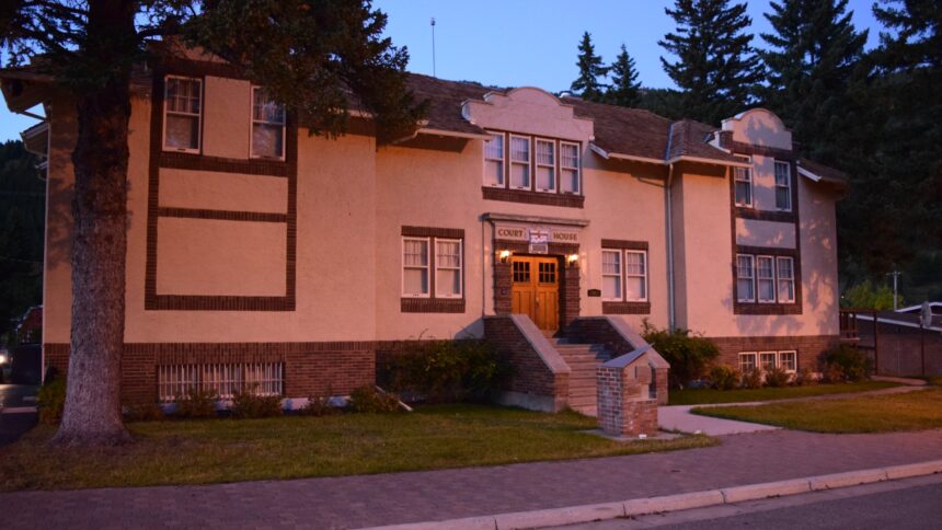 Two-storey buff stucco building with brick trim, a COURT HOUSE sign over the entrance, shaped parapet gables and a tiled roof, photographed at dusk