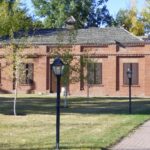 A single-storey red brick building with a lamp post and a paved path in front, framed by trees