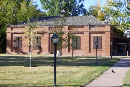 A single-storey red brick building with a lamp post and a paved path in front, framed by trees