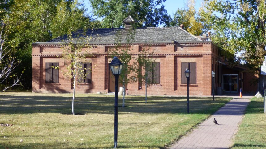 A single-storey red brick building with a lamp post and a paved path in front, framed by trees
