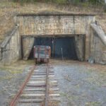 Concrete mine portal with a lettered panel reading Brazeau Collieries Ltd Nordegg No. 2, a chain-link gate, a small ore cart and a rail track running toward the camera