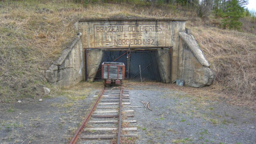 Concrete mine portal with a lettered panel reading Brazeau Collieries Ltd Nordegg No. 2, a chain-link gate, a small ore cart and a rail track running toward the camera