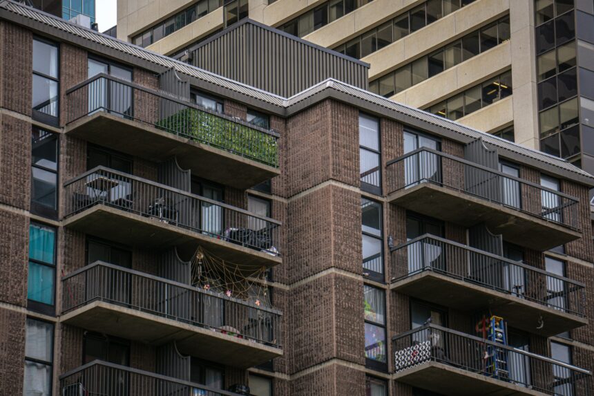 Brown brick apartment building with stacked balconies holding plants, chairs and household items