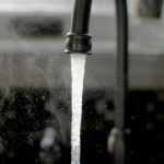 Water running from a dark kitchen tap into a sink