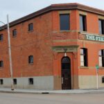 Two-storey red brick building with a cut corner entrance, arched windows and a sign reading The Feedmill across the upper storey, on a street corner in Camrose