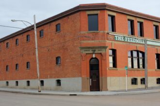 Two-storey red brick building with a cut corner entrance, arched windows and a sign reading The Feedmill across the upper storey, on a street corner in Camrose