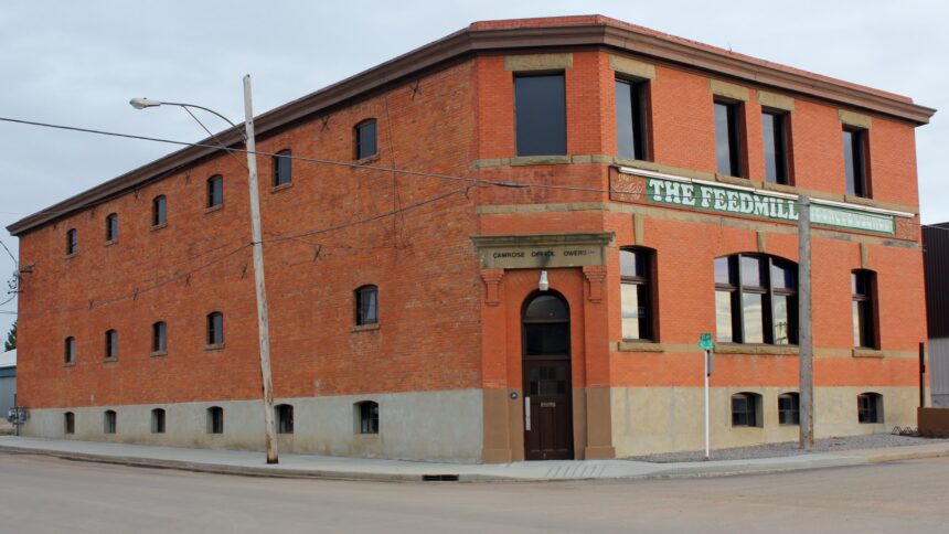 Two-storey red brick building with a cut corner entrance, arched windows and a sign reading The Feedmill across the upper storey, on a street corner in Camrose