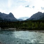 Steel railway bridge crossing the Bow River in Canmore, with the Three Sisters peaks and evergreen forest behind it