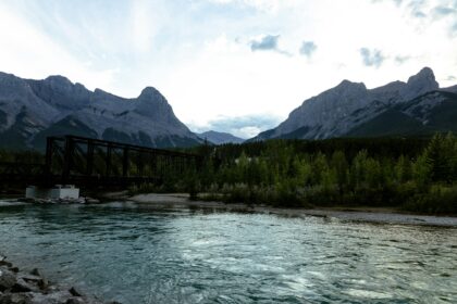 Steel railway bridge crossing the Bow River in Canmore, with the Three Sisters peaks and evergreen forest behind it