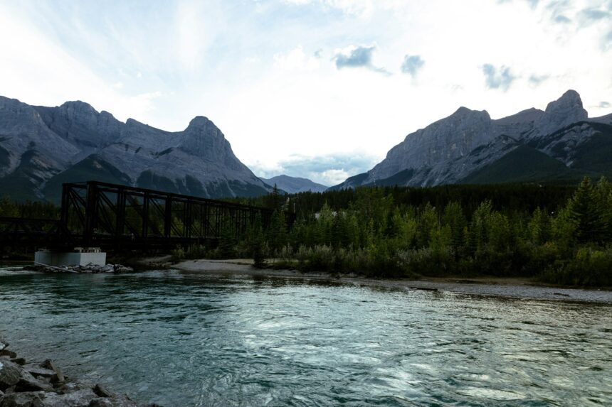 Steel railway bridge crossing the Bow River in Canmore, with the Three Sisters peaks and evergreen forest behind it