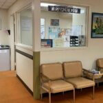 Hospital waiting room with padded chairs beside a reception window