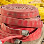 Red and yellow fire hoses coiled and piled on a concrete pad in sunlight