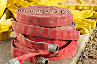 Red and yellow fire hoses coiled and piled on a concrete pad in sunlight
