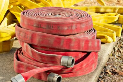 Red and yellow fire hoses coiled and piled on a concrete pad in sunlight