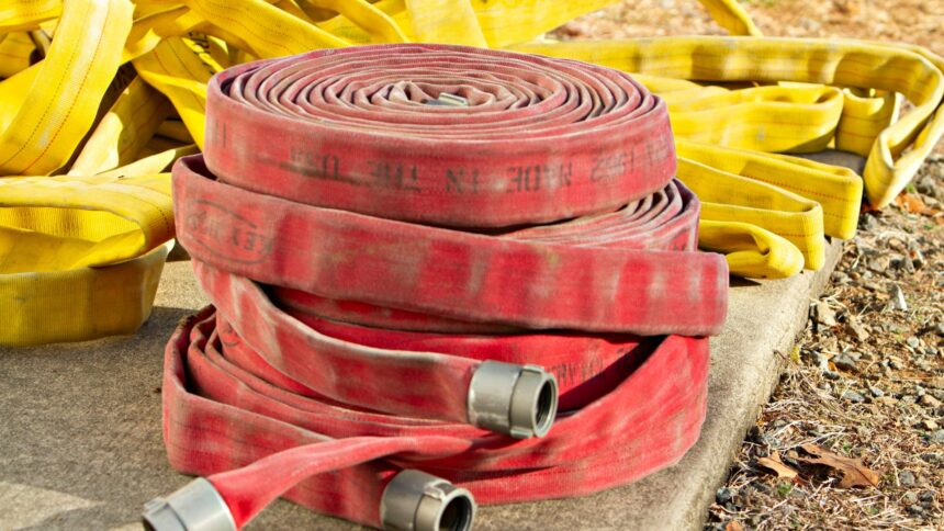 Red and yellow fire hoses coiled and piled on a concrete pad in sunlight