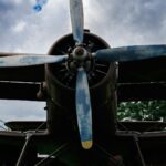 Front view of a vintage biplane with a four-blade propeller under a cloudy sky