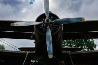 Front view of a vintage biplane with a four-blade propeller under a cloudy sky
