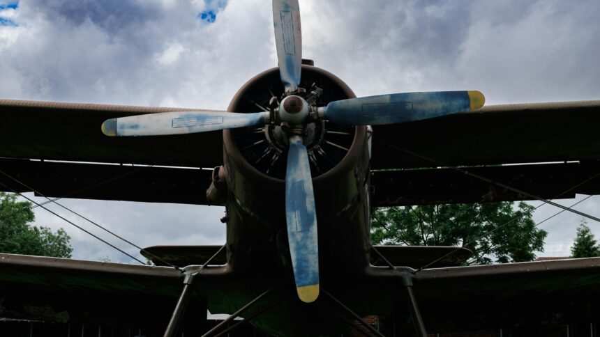 Front view of a vintage biplane with a four-blade propeller under a cloudy sky