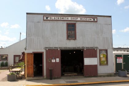 Front of the Lacombe Blacksmith Shop Museum, a corrugated metal building with a Blacksmith Shop Museum sign above open sliding doors