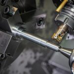 Close-up of a metal rod held in a lathe chuck while a cutting tool machines it