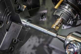 Close-up of a metal rod held in a lathe chuck while a cutting tool machines it