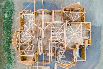 Overhead view of a new house under construction, with wood wall framing and roof trusses laid out across the subfloor