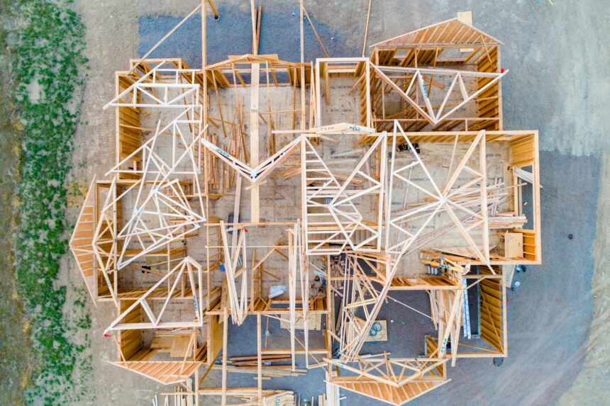 Overhead view of a new house under construction, with wood wall framing and roof trusses laid out across the subfloor