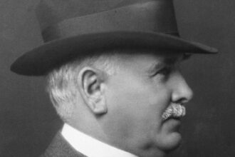 Black and white portrait of Patrick Burns in a hat and suit, shown in profile, photographed in 1927
