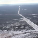 Aerial view of a long straight pipeline right of way cleared through snowy forest, running to the horizon