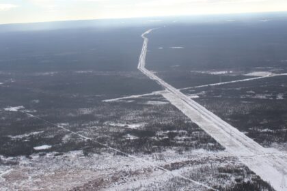 Aerial view of a long straight pipeline right of way cleared through snowy forest, running to the horizon