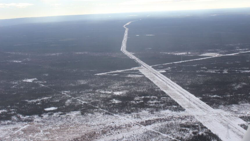 Aerial view of a long straight pipeline right of way cleared through snowy forest, running to the horizon