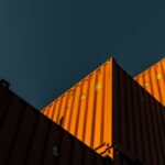 Stacked orange shipping containers seen from below against a dark teal sky