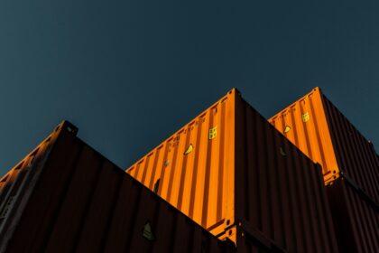 Stacked orange shipping containers seen from below against a dark teal sky