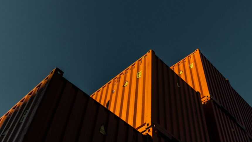 Stacked orange shipping containers seen from below against a dark teal sky