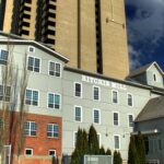 Grey-sided Ritchie Mill with a brick lower storey and the name painted on its wall, beside high-rise towers in Edmonton