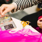 Hands working with bright pink fabric, scissors and a small card on a work table