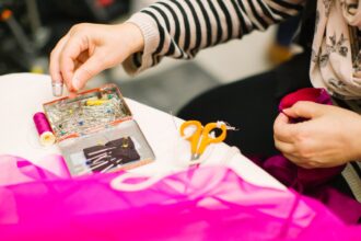 Hands working with bright pink fabric, scissors and a small card on a work table