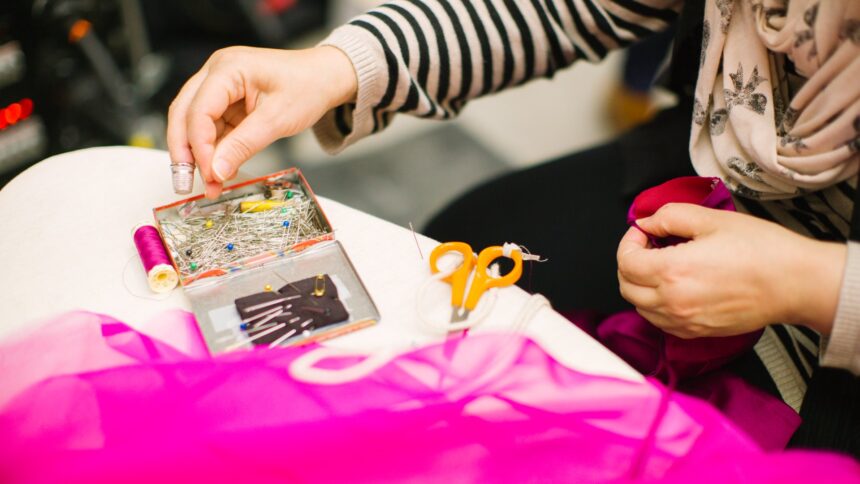 Hands working with bright pink fabric, scissors and a small card on a work table