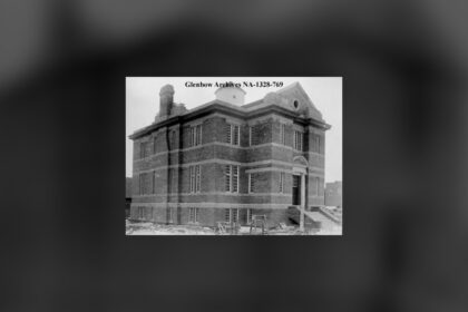 A two-storey brick library building with a tall entrance, standing alone on an open lot, in a black and white 1913 photograph